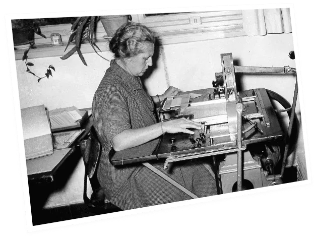 Aufnahme in Schwarz-Weiß von einer Dame, die an einer Braillemaschine arbeitet