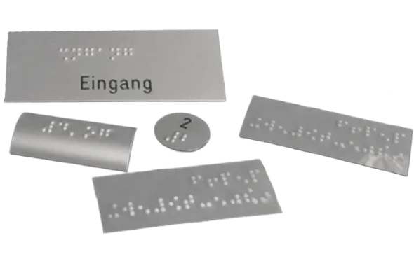 Grau-silberne Schilder in verschiedenen Formen mit Brailleschrift sowie gestanzten Buchstaben und Zahlen